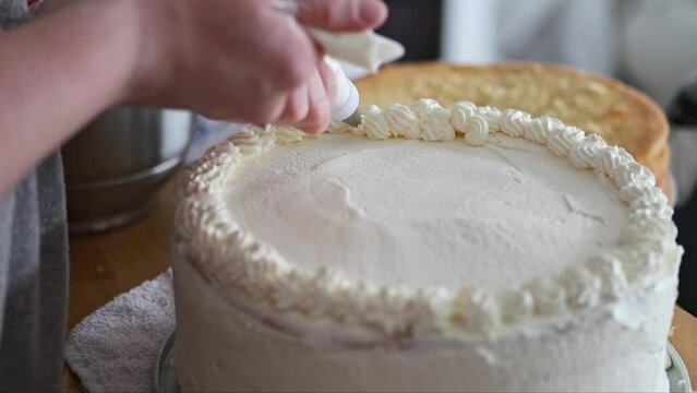 Skilled hands carefully decorate a birthday/wedding cake with creamy layers and toppings. The result is a beautiful and delicious dessert perfect for any celebration.