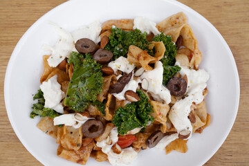 Pasta dish. Top view of a plate with pappardelle noodles, pesto, almonds, kale, burrata cheese and tomatoes, in the restaurant wooden table.