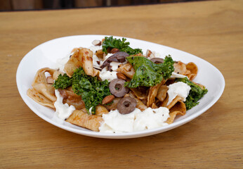 Pasta dish. Closeup view of a plate with pappardelle noodles, pesto, almonds, kale, burrata cheese and tomatoes, in the restaurant wooden table.