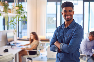 Portrait Of Young Smiling Businessman Standing In Modern Office 