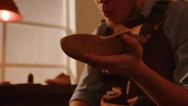 Craftsman grinds wooden shoe last with sandpaper in shoemaker workshop. Handmade shoe making.  - Powered by Adobe