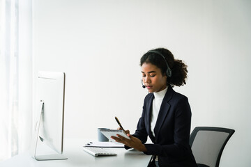 African american woman in headset writing notes while talking support customer in call center