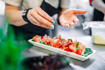 Chef decorate ready dish with slices parma ham on restaurant kitchen
