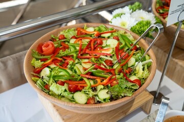 beautiful and colorful salad filled with lettuce greens cucumbers tomatoes red and green peppers at a catering event