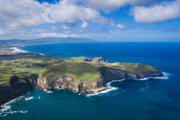 Fototapeta na wymiar Aerial view of the coastline on Sao Miguel Island, with town buildings, green farmland and volcanic mountains, Azores, Portugal