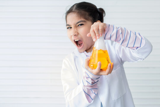 Cheerful Asian school girl wearing lab coat showing yellow liquid in beaker on white wall,  learning chemistry in laboratory at school