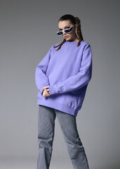 a fashionable woman in stylish sunglasses and a lilac hoodie poses on a gray background
