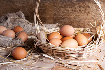 Close-up shot of fresh eggs and hen eggs with dried straw lying on wooden table in organic farm.