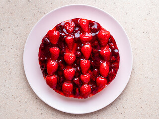 top view of sweet cake with strawberries and cherries on pink plate and pink stone board