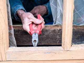 repair of wooden window frame in rural house with pliers close up