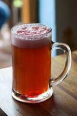 Mug of sweet cold light beer with pomegranate juice and foam on the restaurant table. Real life photography at a restaurant, sunny day, light cold beer on the table, close up.
