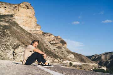 Naklejka premium Young man sitting on asphalt road in sunlight
