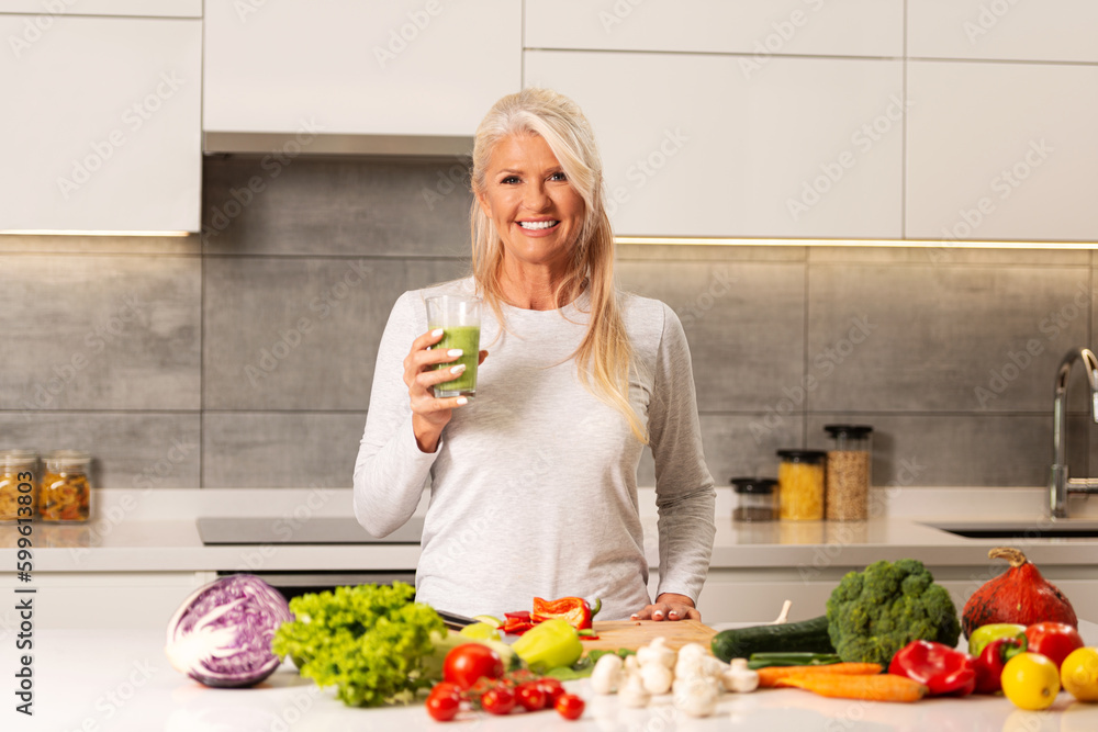 Wall mural beautiful, older woman making a healthy green - fruit and vegetable smoothie.