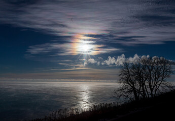 Fototapeta na wymiar Frozen steamy lake with clouds and sun dog