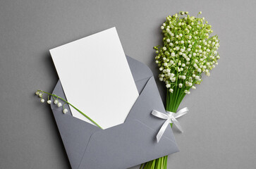 Invitation or greeting card mockup with envelope and lily of the valley flowers, flat lay on grey...