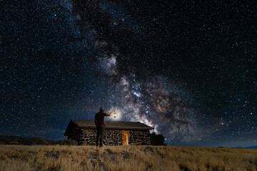 Young man holding up a lantern by a ghost town cabin with the nighttime Milky Way in the sky