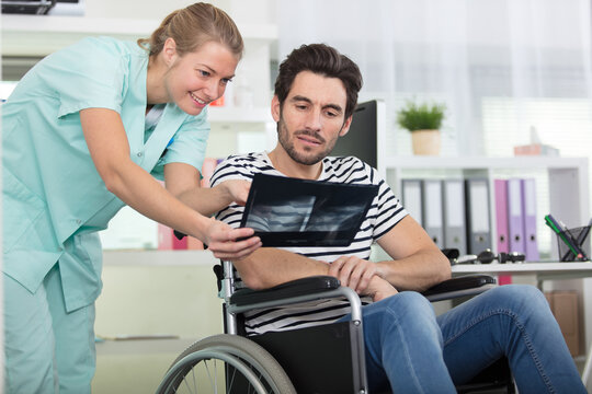young female medic holding x-ray image showing to disabled patient
