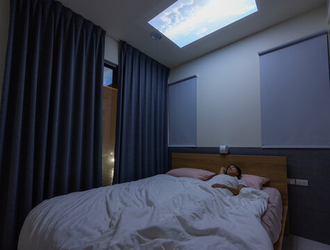 Woman lying down on bed and watch the video project on the ceiling at home
