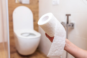 woman's hand tears off roll of white toilet paper close-up. bathroom background