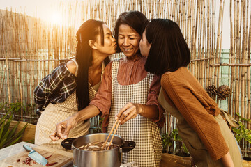 Southeast asian mother with her daughters having fun preparing Thai food recipe together at house patio