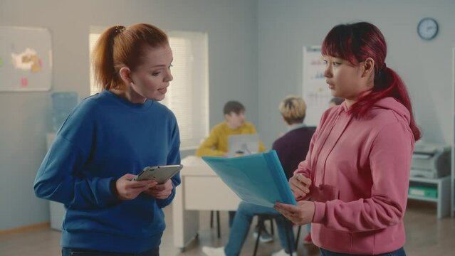 Young European and Asian women are discussing a new business project, getting angry and quarreling, comparing data in a digital tablet and a document. Group of managers working together in office.