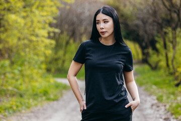 Stylish brunette asian girl wearing black t-shirt posing against nature