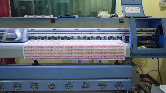 Large format inkjet printer printing on sticker sheet with branding and technician working in workplace