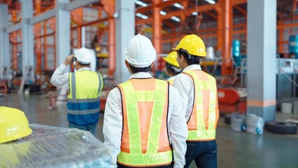 Back view of team warehouse workers in safety uniform walking at industry manufacturing factory. Teamwork concept