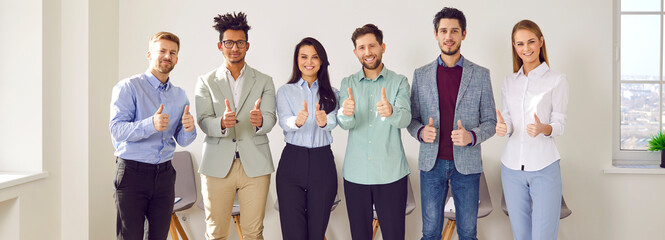 Happy, joyful business team giving thumbs up together. Banner with a group portrait of cheerful, smiling mixed race men and women standing in the office and doing like gestures. Success concept