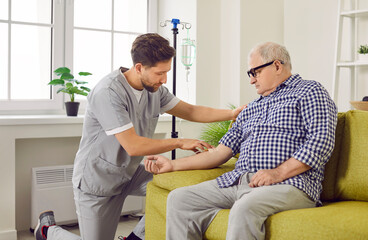 Nurse or doctor giving intravenous infusion to elderly patient. Young man in uniform inserts IV...