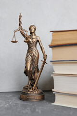 themis goddess of justice statuette on background of books on desktop. symbol of law with scales and sword in his hands. legal company or university of law and judicial structure. library education