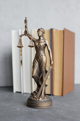 themis goddess of justice statuette on background of books on desktop. symbol of law with scales and sword in his hands. legal company or university of law and judicial structure. library education
