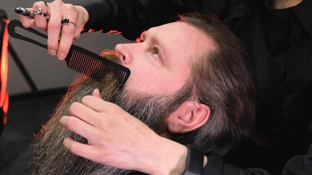 a hairdresser girl makes a beard styling for a man
