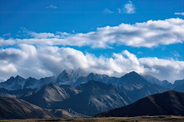 Fototapeta premium view of majestic mountain range, with clear blue skies and fluffy clouds overhead, created with generative ai