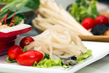 Close up of white pho big noodle on dish with red tomato and various vegetable in background