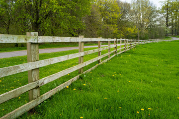 Large wooden fence seen at the perimeter for a large meadow with a public path seen following the...