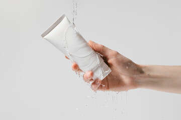 Female hand holding white mockup tube of moisturizer under water on white isolated background....