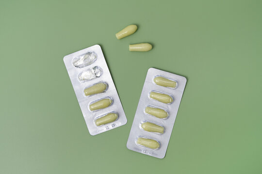 Green rectal pills or suppositories for anal or vaginal use with blister on green isolated background. Medicines for alternative medicine, lowering temperature, hemorrhoids and healthy concept