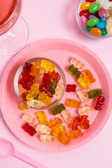 Plate with gummy bears, jelly beans and a glass with a pink drink on a pink table. Coloring in food. Parties and celebrations