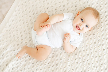 close-up of a laughing happy baby on a white cotton bed in a bright bedroom, a small smiling baby...