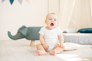 Naklejka premium cute little baby boy in the children's bright room yawns in a cotton bodysuit and wants to sleep