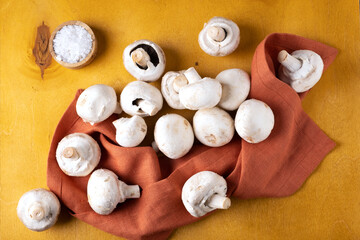 Close-up of champignon mushrooms on a linen napkin on a yellow background. Selective focus.