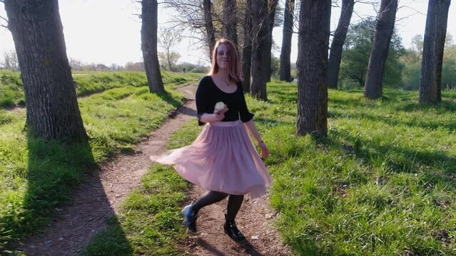 woman in a park spinning on a footpath and smiling on a sunny day