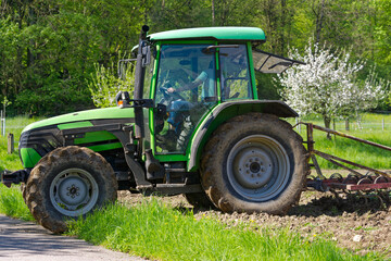 Close-up of green tractor  with female driver ploughing agriculture field at City of Zürich on a sunny spring day. Photo taken May 4th, 2023, Zurich, Switzerland.