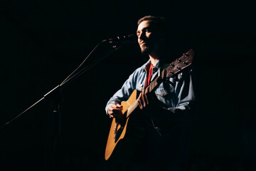 The singer plays an acoustic guitar and sings at a concert