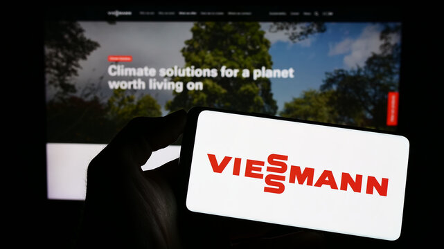 Stuttgart, Germany - 04-28-2023: Person holding mobile phone with logo of German company Viessmann Group GmbH Co. KG on screen in front of web page. Focus on phone display.