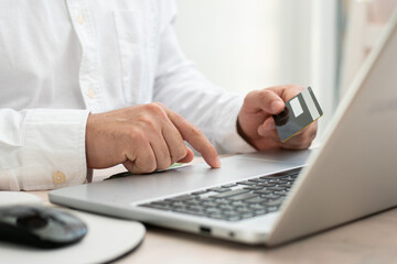 Close up of person touching their laptop while hold a credit card front the laptop for online...