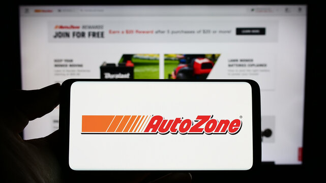 Stuttgart, Germany - 04-28-2023: Person holding cellphone with logo of US automotive parts company AutoZone Inc. on screen in front of business webpage. Focus on phone display.