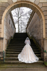 the bride walks along the stone steps of an ancient building, a palace in an arch. Rear view, from the back. The bride is wearing a beautiful long dress. Wedding