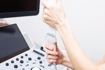 Woman doctor's hand applies a medical gel to ultrasonic sensor of ultrasound machine in the clinic.
